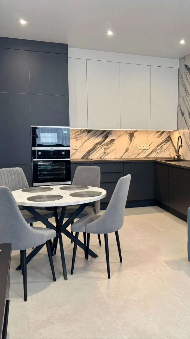 Modern dark gray kitchen with dramatic marble slab backsplash and round dining table