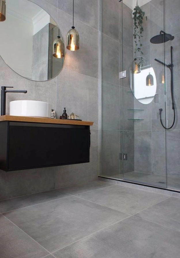 Sleek bathroom with large-format gray concrete-look tiles, round mirror, and black fixtures