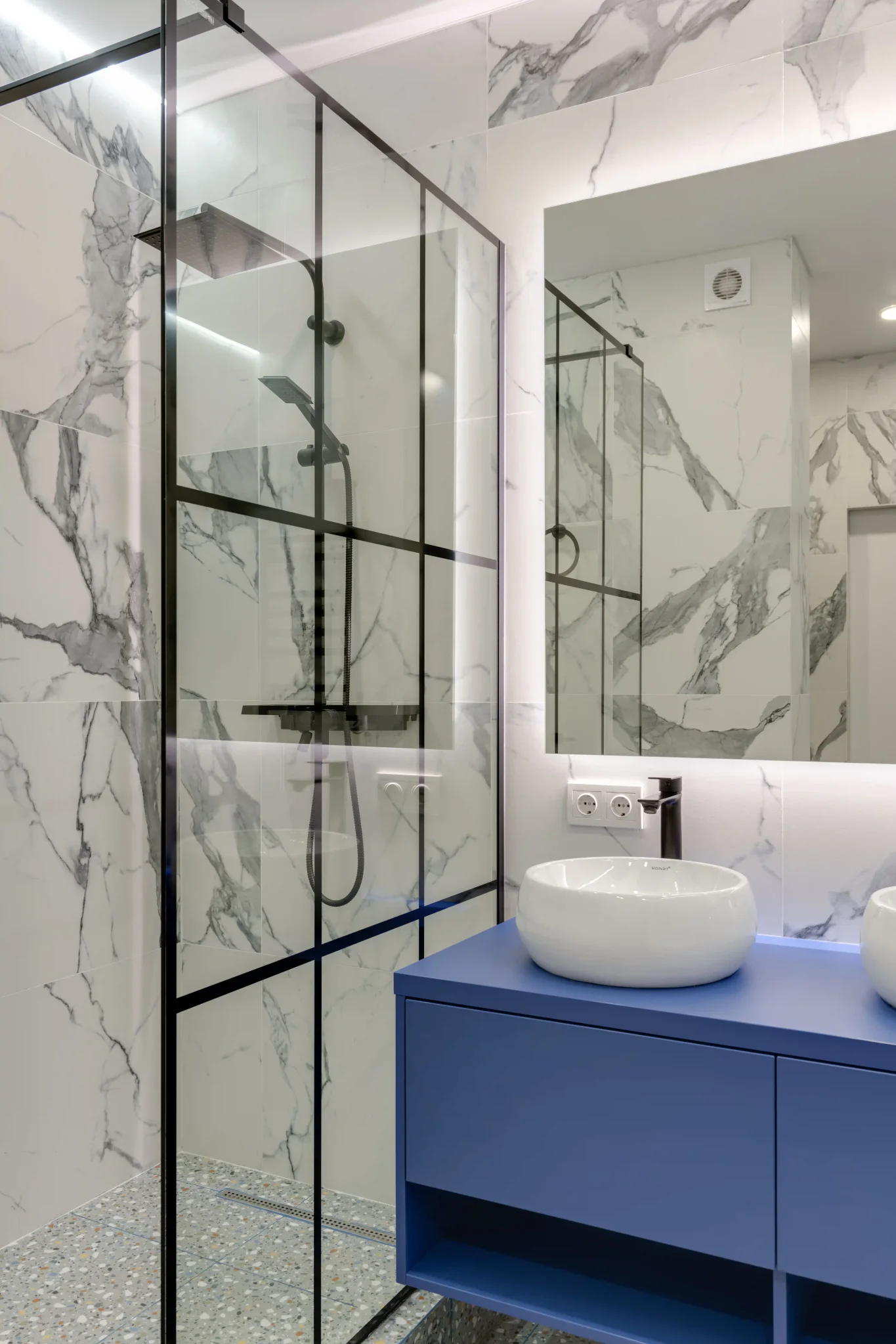 Modern bathroom with white marble wall tiles, blue vanity cabinet, and glass shower enclosure