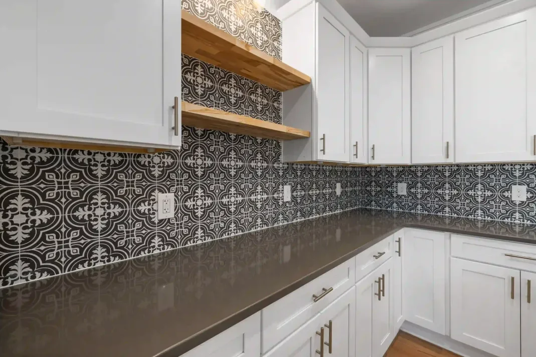White kitchen with bold black and white patterned encaustic tile backsplash and wood shelves