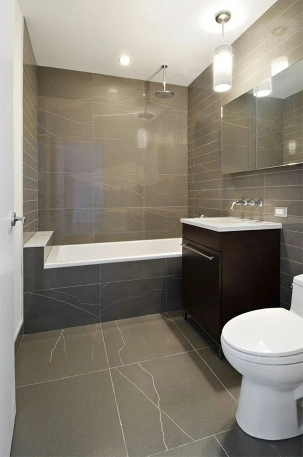 Modern bathroom with large-format taupe stone-look tiles surrounding a built-in bathtub in Carson